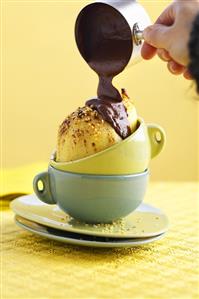 Pouring chocolate sauce over poached pear & sesame seeds