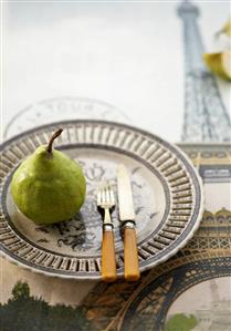 A pear on a plate with a knife and fork