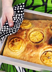 Woman holding a lemon focaccia on a baking tray