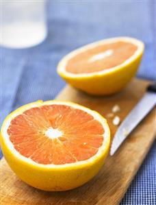 Halved pink grapefruit on chopping board with knife