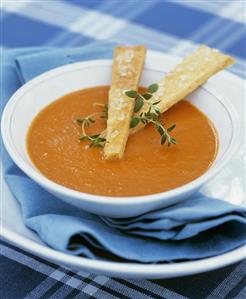 A plate of carrot soup with fresh thyme and bread sticks