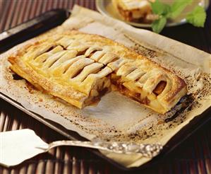 Apple strudel on baking tray, a piece taken