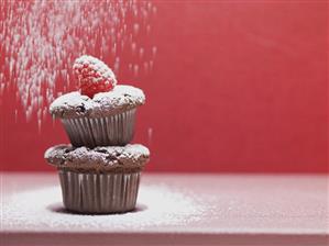 Two chocolate muffins being sprinkled with icing sugar