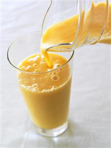 Pouring orange yoghurt drink from a jug into a glass