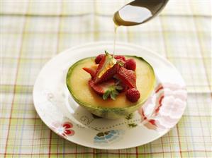 Honey being poured over fresh berries on Charentais melon