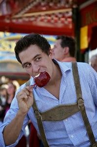 Man in lederhosen eating toffee apple