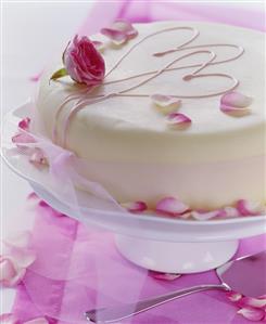 White cake with rose petals, pink hearts and bow