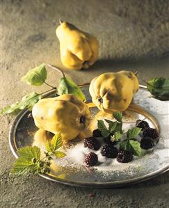 Pear-shaped quinces and blackberries with sugar on a tray