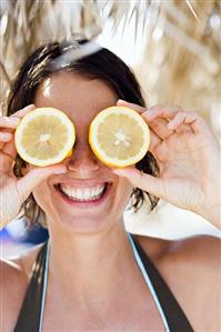 Young woman holding two lemon halves in front of her eyes