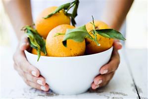 Hands holding a bowl of fresh oranges