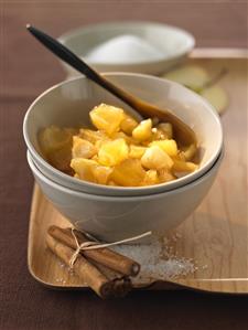 Baked apple jam in bowl, cinnamon sticks, sugar