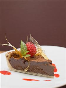 Piece of chocolate tart with caramel fan and raspberry