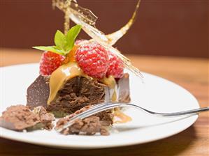 Piece of chocolate tart with raspberries & caramel (partly eaten)