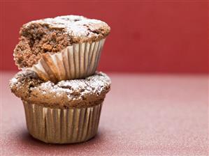 Two chocolate muffins with icing sugar, one partly eaten