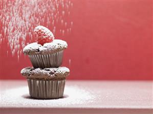 Sprinkling two chocolate muffins with icing sugar