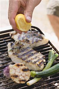 Hand squeezing lemon juice over grilled fish fillets