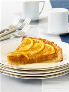 A piece of orange and almond tart on a pile of plates