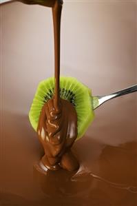 Coating a slice of kiwi fruit in couverture chocolate