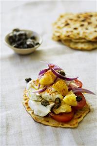 Naan bread topped with tomato, pineapple and capers