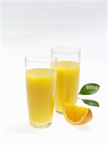 Two glasses of orange juice, wedge of orange and leaves