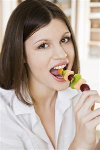 Young woman eating fruit skewer