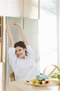 Young woman stretching at breakfast table