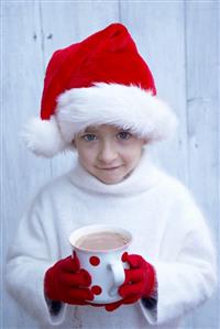 Small boy in Father Christmas holding mug of hot chocolate