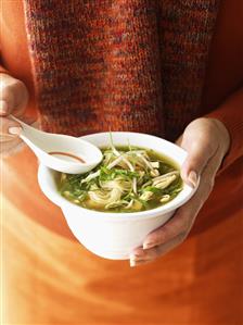 Woman holding bowl of chicken noodle soup