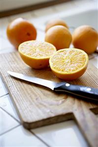 Oranges, whole and halved, on chopping board with knife