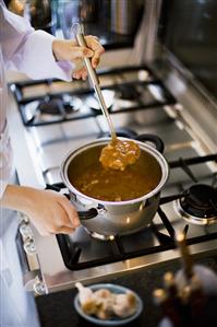 Female chef making vegetable soup on gas cooker