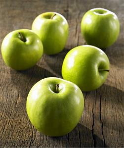 Five Granny Smith apples on wooden background