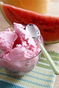 Watermelon ice cream in a dish, slice of watermelon behind