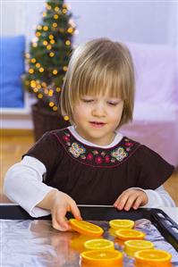 Little girl laying orange slices on a baking tray
