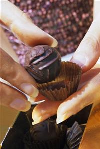 Hands holding a chocolate with a paper case