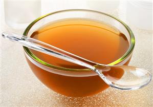 Beef stock in a glass bowl with a plastic spoon