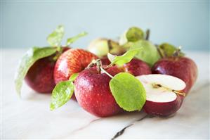 Several whole red apples and one half with leaves