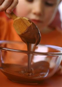 Small girl stirring chocolate cream with wooden spoon