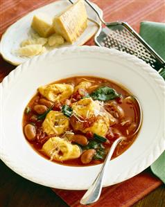 White Bowl of Tortellini Tomato Soup with a Spoon; Parmesan Cheese and Cheese Grater