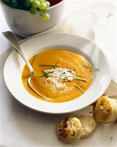 Bowl of Creamy Squash Soup with a Spoon; Biscuits