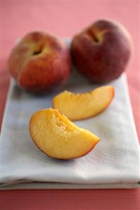 Two Peach Slices and Two Whole Peaches on a Folded Dish Cloth