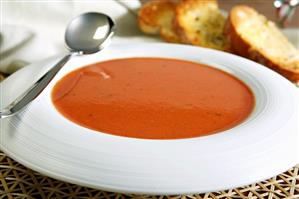 A Bowl of Creamy Tomato Soup with Spoon and Bread