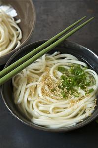 Bowl of Udon Soup with Green Onion and Sesame Seeds; Chopsticks