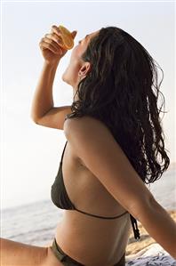 Young woman on beach squeezing an orange into her mouth