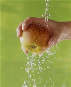 A Hand Holding an Apple Under a Stream of Water