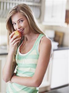 Teenage girl in kitchen eating an apple