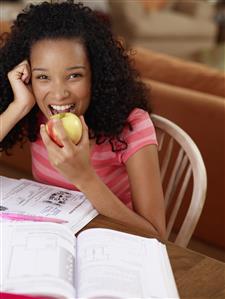 Teenage girl sitting at table with homework eating an apple