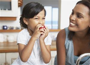 Mother in kitchen with daughter eating red apple