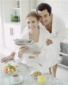 Man and woman in bathrobes with healthy breakfast reading newspaper