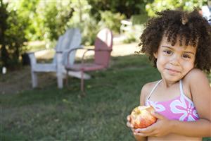 Girl in swimwear holding apple in yard