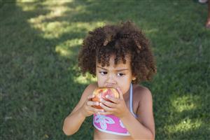 Girl in swimwear eating apple in yard